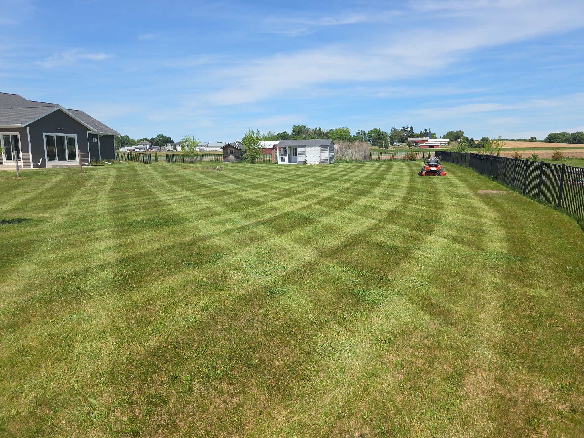 Large fenced backyard freshly mowed with a zero-turn mower